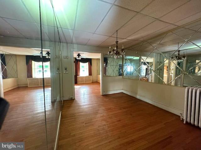 unfurnished dining area with ceiling fan with notable chandelier, wood-type flooring, and radiator