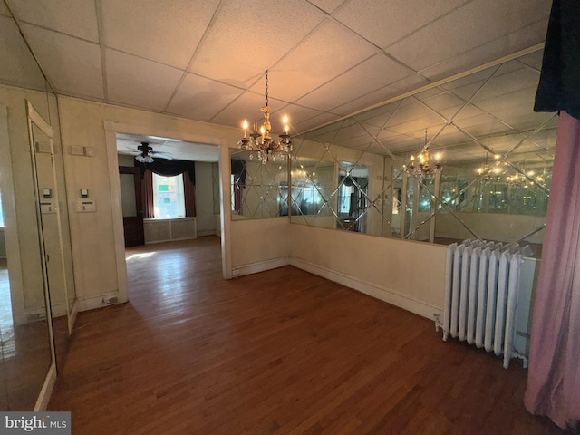 unfurnished dining area featuring hardwood / wood-style flooring, ceiling fan with notable chandelier, a paneled ceiling, and radiator heating unit