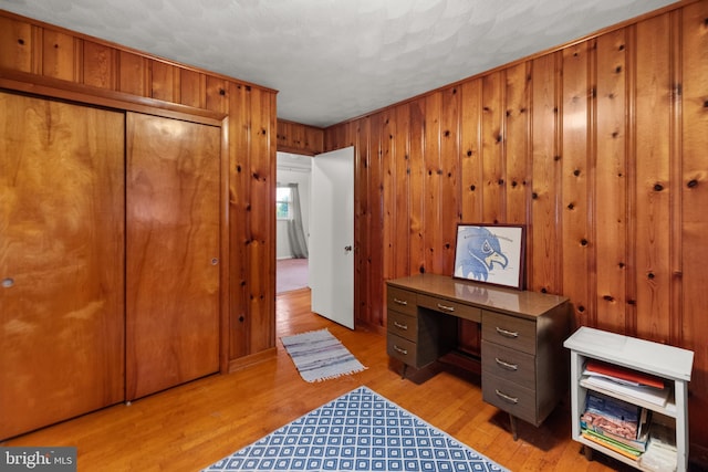 office with light wood-type flooring, a textured ceiling, and wooden walls