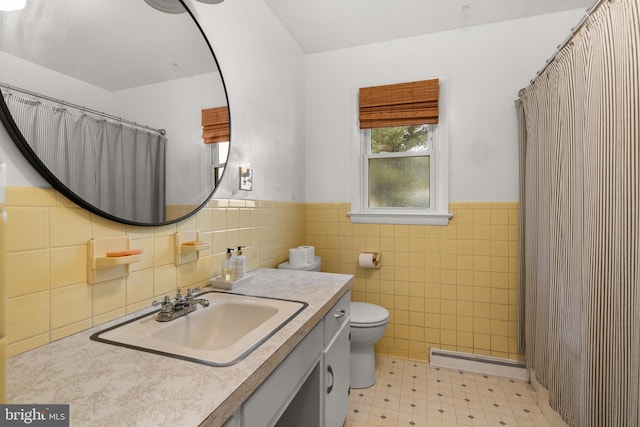 bathroom featuring vanity, toilet, baseboard heating, and tile walls