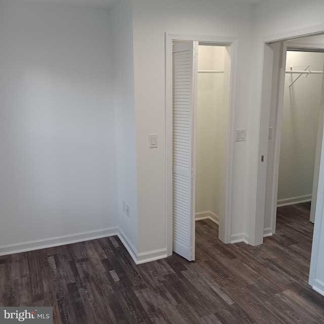 unfurnished bedroom featuring dark wood-type flooring, a closet, a walk in closet, and baseboards