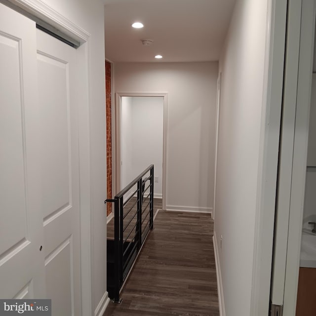 hall with an upstairs landing, recessed lighting, dark wood-style flooring, and baseboards