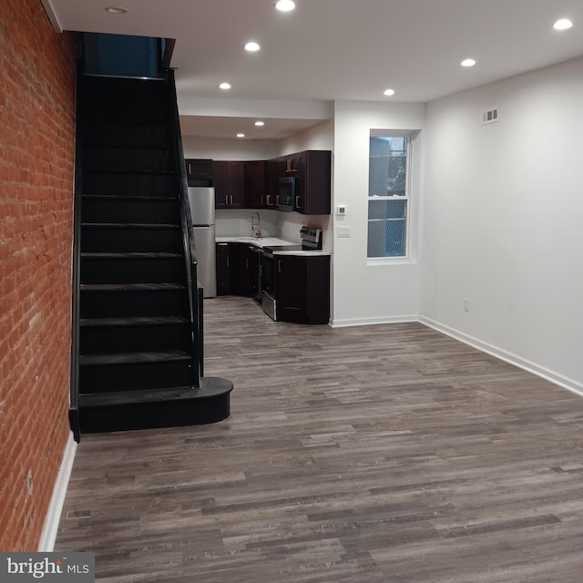 kitchen featuring sink, light hardwood / wood-style flooring, appliances with stainless steel finishes, dark brown cabinetry, and brick wall