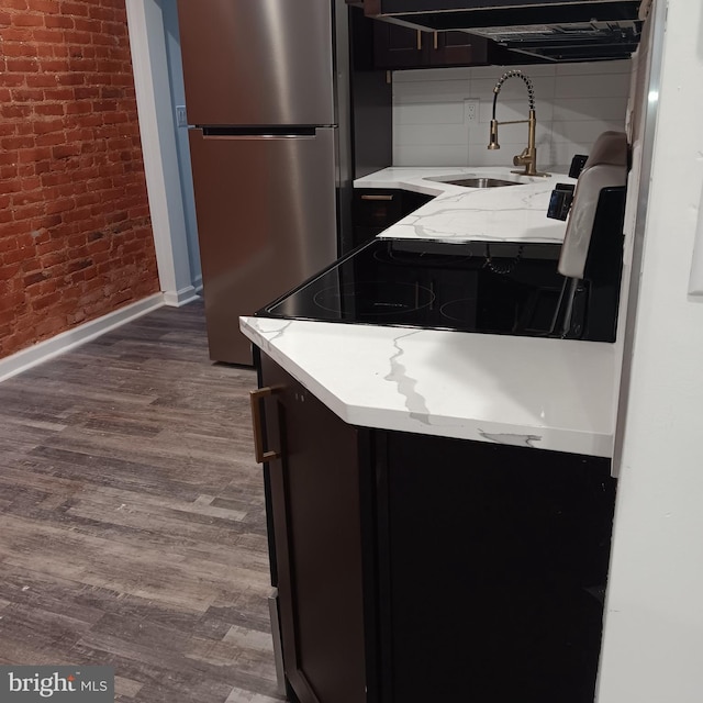 kitchen with dark wood-type flooring, sink, stainless steel refrigerator, light stone counters, and brick wall