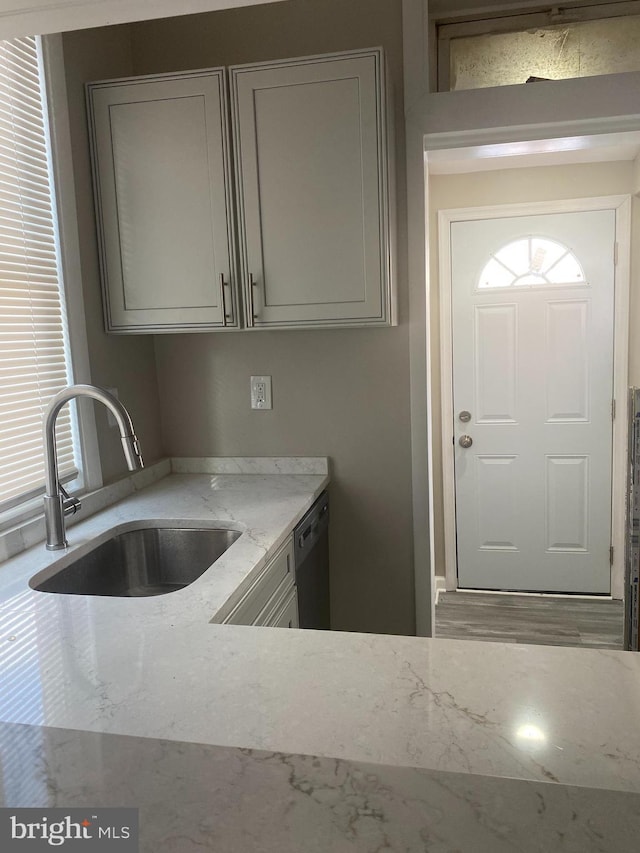 kitchen with light stone countertops, sink, and black dishwasher