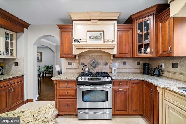 kitchen with light wood-type flooring, custom range hood, backsplash, and stainless steel range with gas cooktop