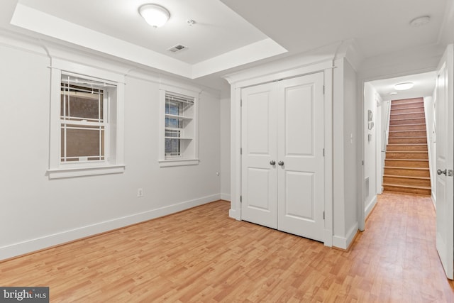 unfurnished bedroom featuring a closet, a tray ceiling, and light hardwood / wood-style flooring