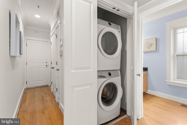 clothes washing area featuring light hardwood / wood-style flooring, stacked washer / dryer, and ornamental molding