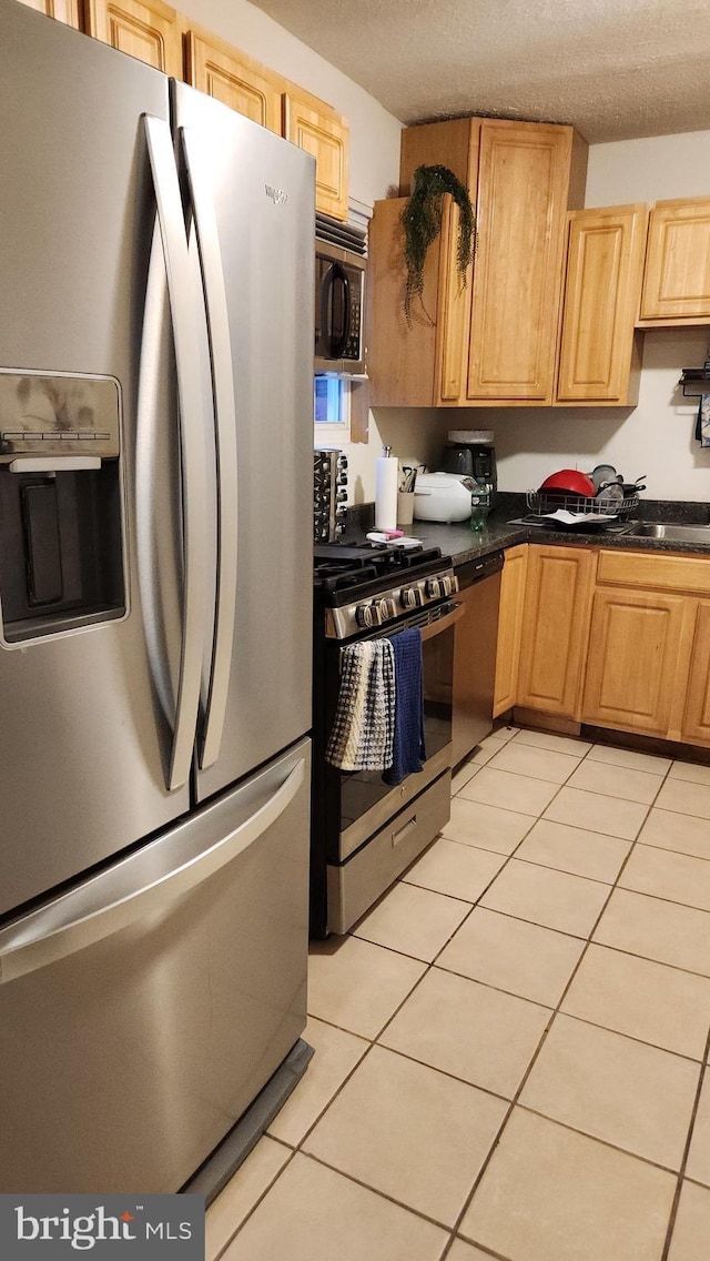 kitchen with a textured ceiling, sink, light tile patterned floors, and stainless steel appliances