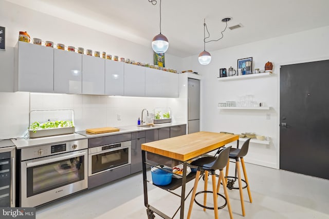 kitchen featuring white cabinetry, stainless steel oven, sink, backsplash, and decorative light fixtures