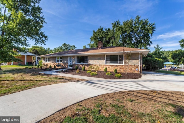 ranch-style house featuring a front yard, concrete driveway, brick siding, and a chimney