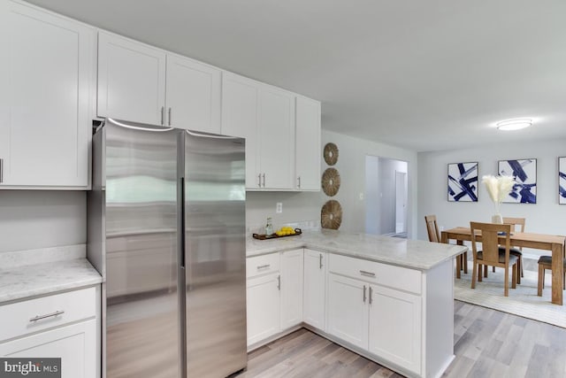 kitchen with a peninsula, light wood-style flooring, white cabinetry, and freestanding refrigerator