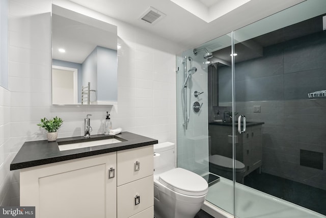 bathroom with vanity, toilet, tile walls, and a shower with shower door