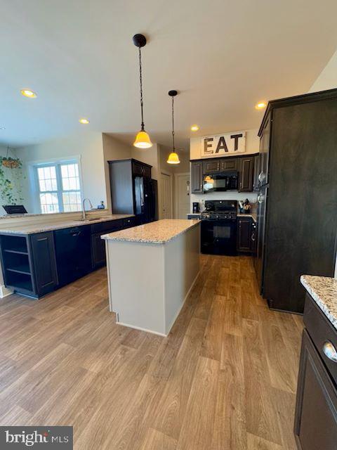 kitchen featuring a kitchen island, hanging light fixtures, light hardwood / wood-style floors, black appliances, and dark brown cabinets