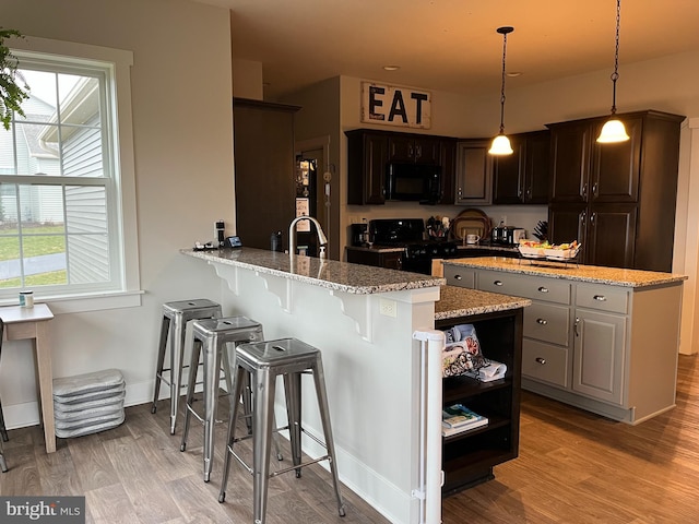 kitchen featuring pendant lighting, black appliances, kitchen peninsula, light stone countertops, and dark brown cabinets