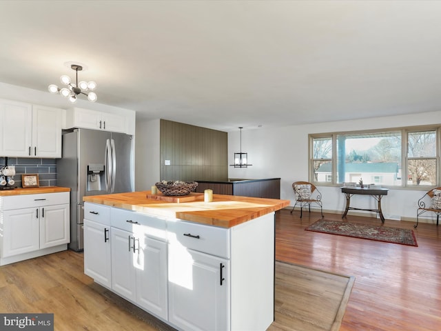 kitchen with wood counters, stainless steel refrigerator with ice dispenser, pendant lighting, white cabinets, and light hardwood / wood-style floors