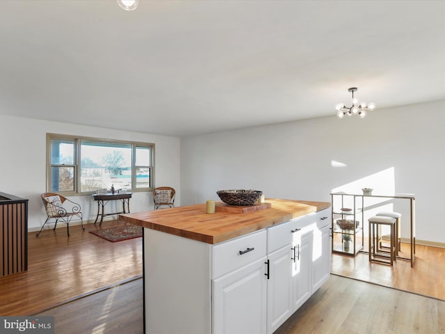 kitchen with wood counters, a kitchen island, light hardwood / wood-style flooring, white cabinetry, and hanging light fixtures