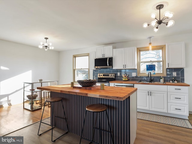 kitchen with stainless steel appliances, decorative light fixtures, a chandelier, white cabinetry, and butcher block counters