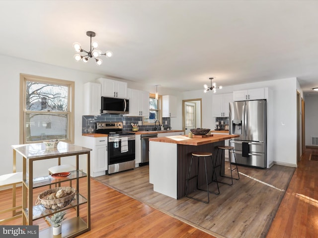 kitchen with stainless steel appliances, decorative light fixtures, an inviting chandelier, white cabinets, and a kitchen island