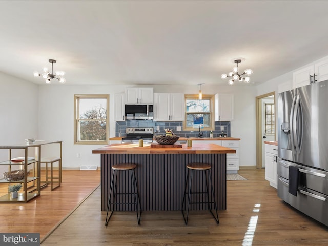 kitchen featuring white cabinetry, hanging light fixtures, stainless steel appliances, an inviting chandelier, and wooden counters