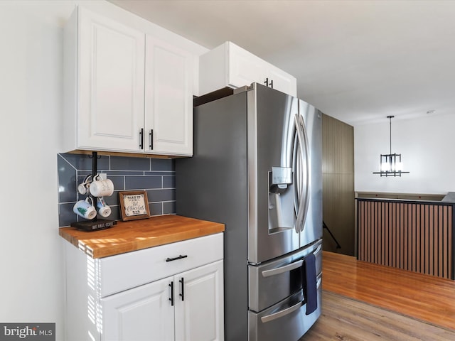 kitchen with stainless steel refrigerator with ice dispenser, butcher block countertops, decorative light fixtures, light hardwood / wood-style floors, and white cabinetry