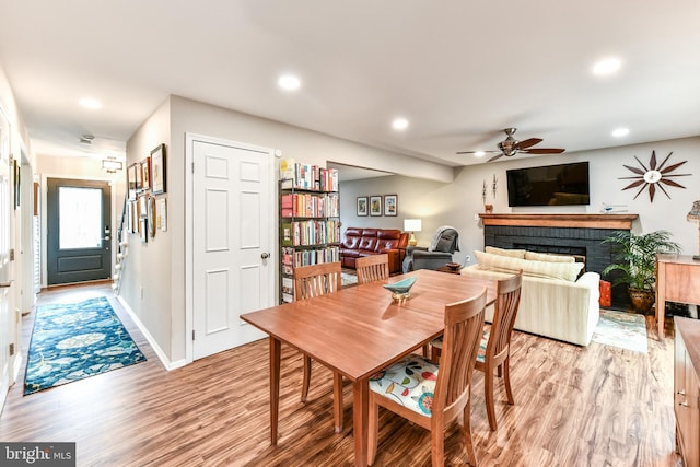 dining area featuring ceiling fan, a brick fireplace, and light wood-type flooring