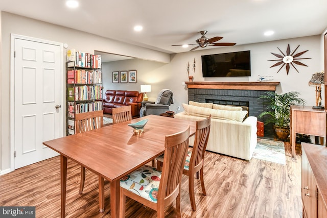 dining room with ceiling fan, a brick fireplace, and light hardwood / wood-style floors