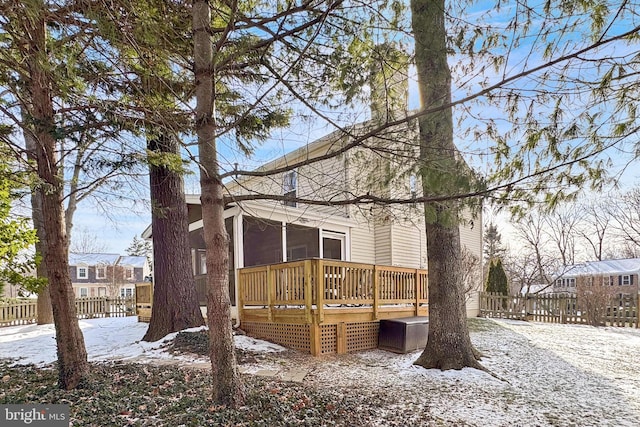 snow covered back of property with a wooden deck and a sunroom