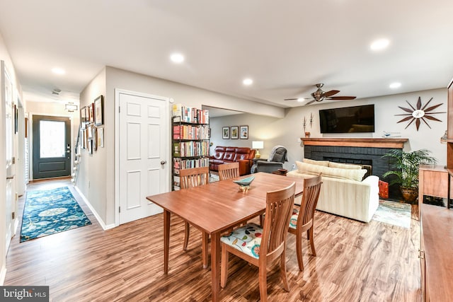 dining room featuring a brick fireplace, ceiling fan, and light wood-type flooring