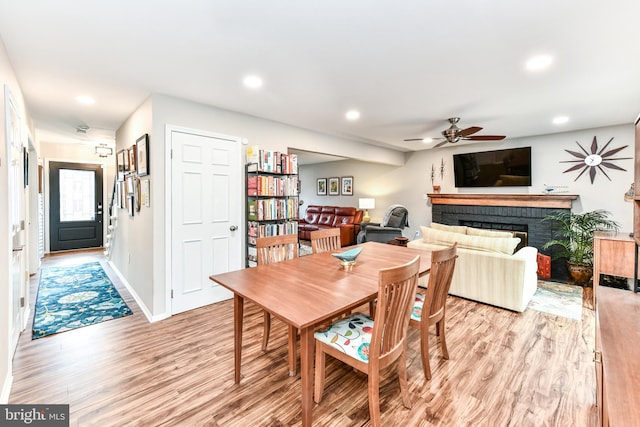 dining space featuring ceiling fan, a brick fireplace, and light hardwood / wood-style flooring