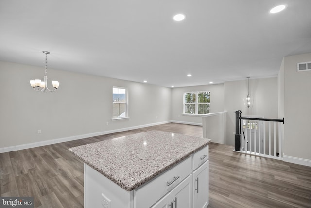 kitchen with hardwood / wood-style floors, white cabinets, light stone countertops, decorative light fixtures, and a kitchen island