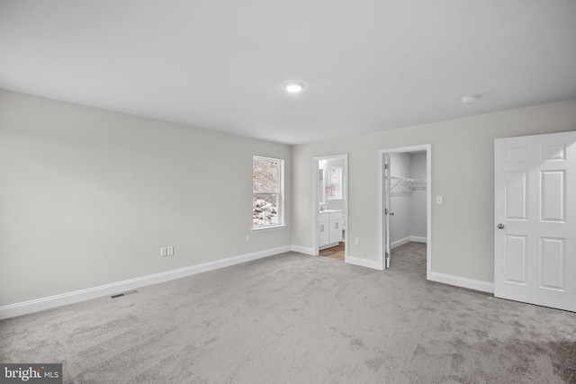 unfurnished bedroom featuring light carpet, a closet, a spacious closet, and ensuite bath