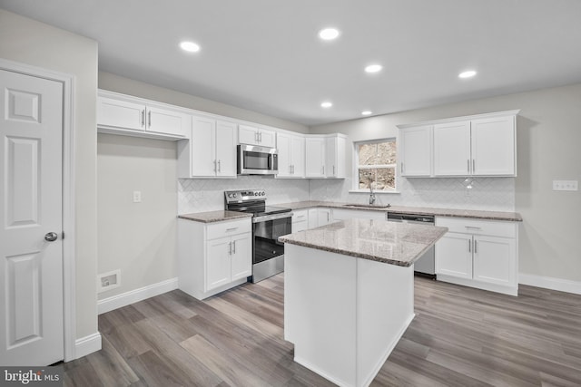 kitchen featuring light stone countertops, stainless steel appliances, a kitchen island, light hardwood / wood-style flooring, and white cabinets