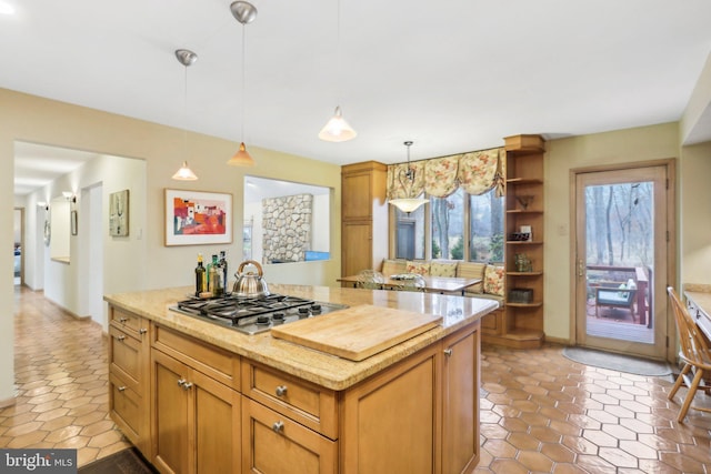 kitchen featuring stainless steel gas stovetop, a center island, light stone countertops, and hanging light fixtures