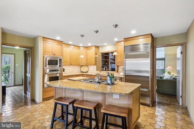 kitchen with built in appliances, pendant lighting, decorative backsplash, light brown cabinetry, and a kitchen island