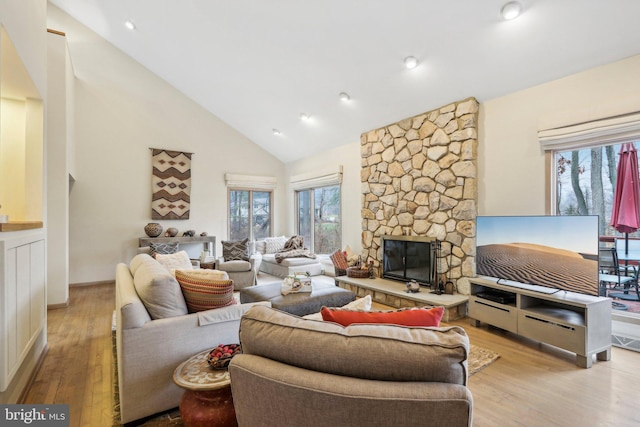 living room featuring plenty of natural light, a stone fireplace, light wood-type flooring, and high vaulted ceiling