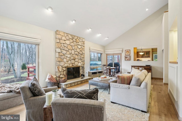 living room with a fireplace, high vaulted ceiling, and light hardwood / wood-style flooring