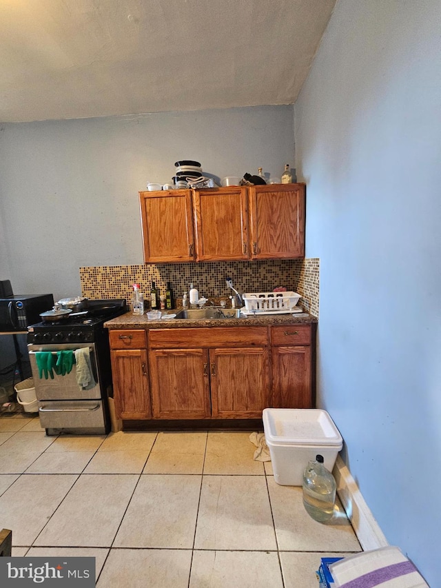 kitchen with stainless steel gas stove, sink, light tile patterned floors, and backsplash