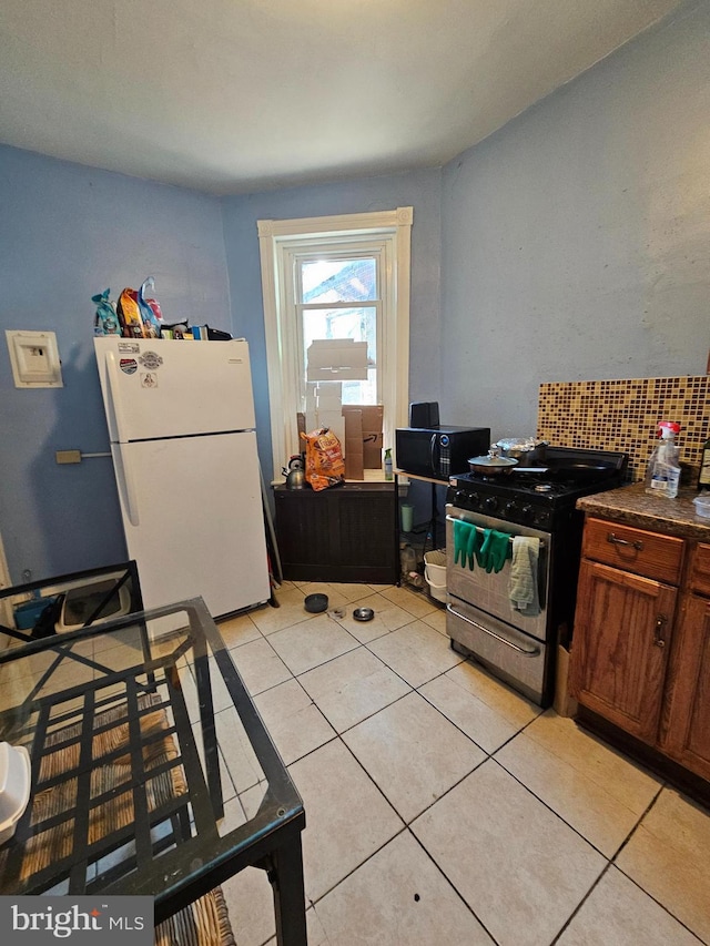 kitchen with light tile patterned floors, white refrigerator, backsplash, and stainless steel range with gas stovetop