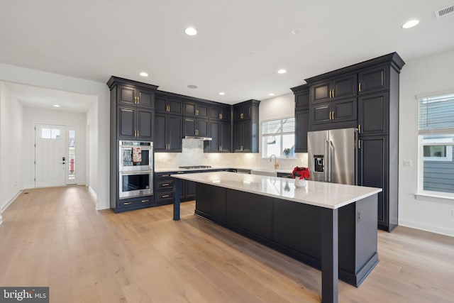 kitchen with decorative backsplash, appliances with stainless steel finishes, light hardwood / wood-style flooring, a center island, and a breakfast bar area