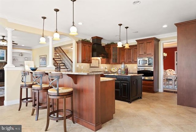 kitchen with light stone countertops, stainless steel appliances, an island with sink, decorative light fixtures, and custom exhaust hood