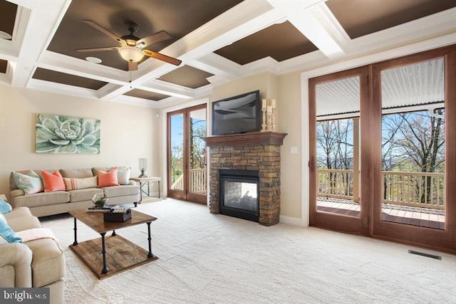 carpeted living room with beam ceiling, a stone fireplace, ceiling fan, and coffered ceiling