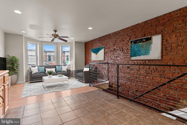 living room featuring hardwood / wood-style flooring, ceiling fan, and brick wall