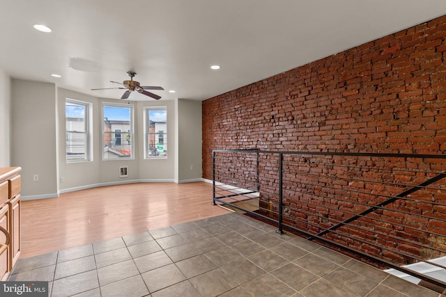 unfurnished living room featuring ceiling fan, hardwood / wood-style floors, and brick wall