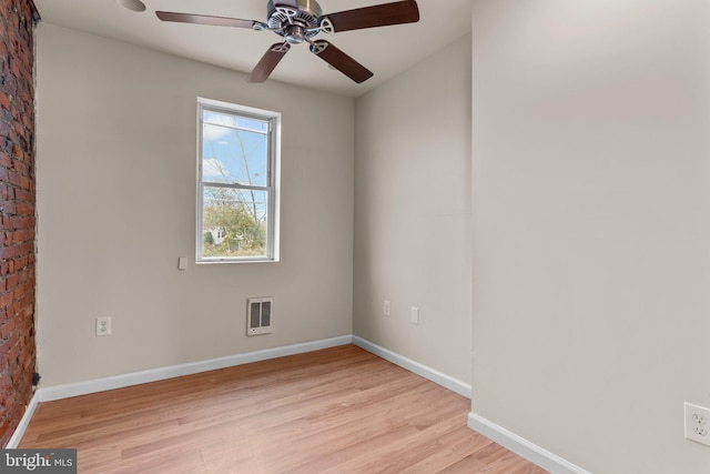 empty room with ceiling fan, light hardwood / wood-style floors, and brick wall