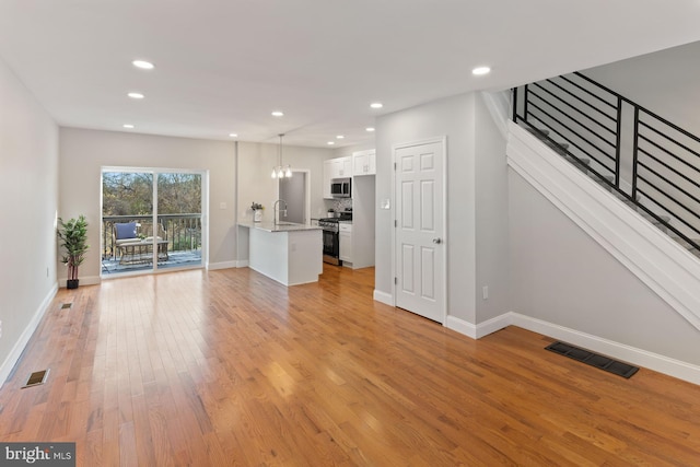 unfurnished living room with a notable chandelier, light wood-type flooring, and sink