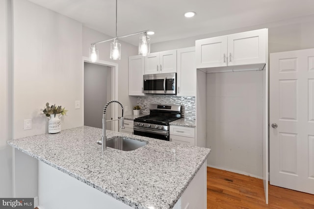 kitchen with kitchen peninsula, stainless steel appliances, sink, decorative light fixtures, and white cabinets