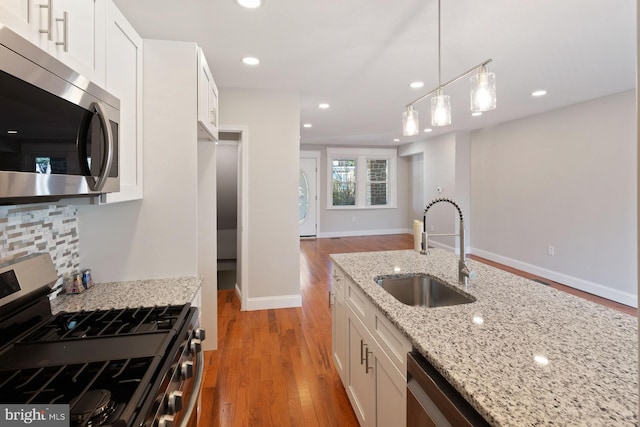 kitchen with light stone countertops, appliances with stainless steel finishes, white cabinets, and sink