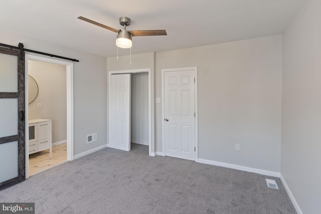 unfurnished bedroom with light carpet, a barn door, and ceiling fan