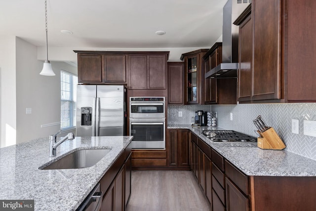 kitchen featuring light stone countertops, stainless steel appliances, wall chimney range hood, sink, and light hardwood / wood-style flooring